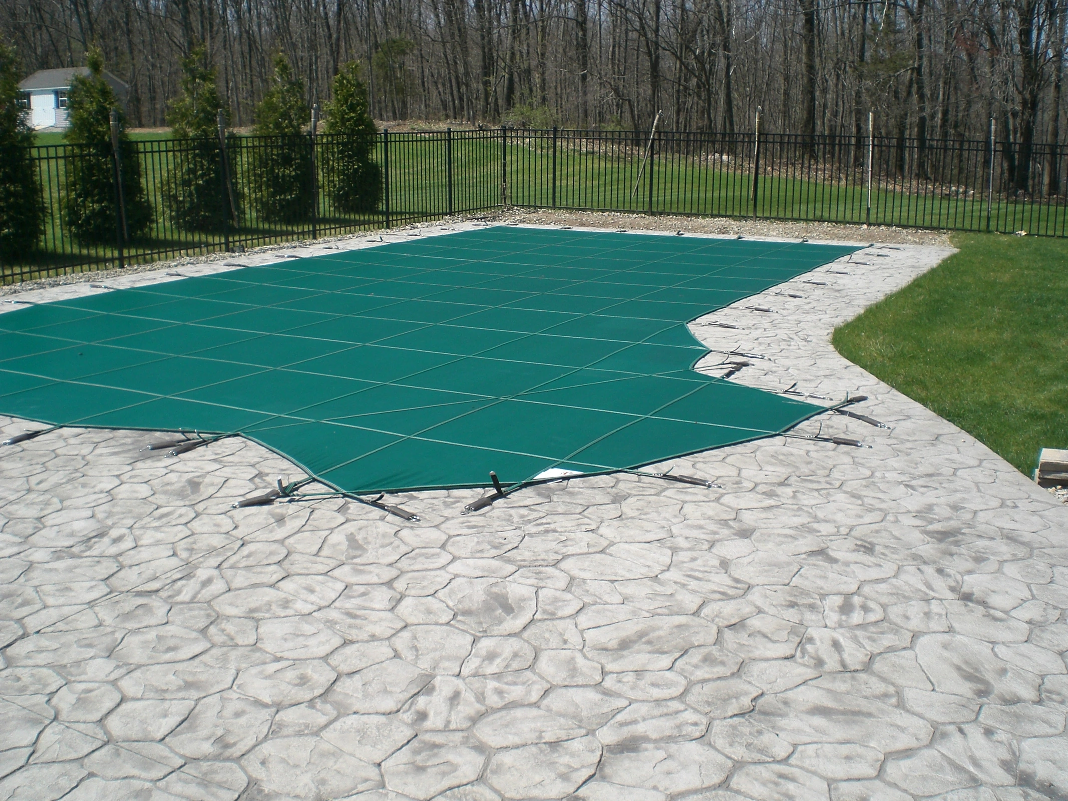 J-PAC Construction stamped random stone concrete pool patio with safety cover installation and black perimeter fencing in Maine