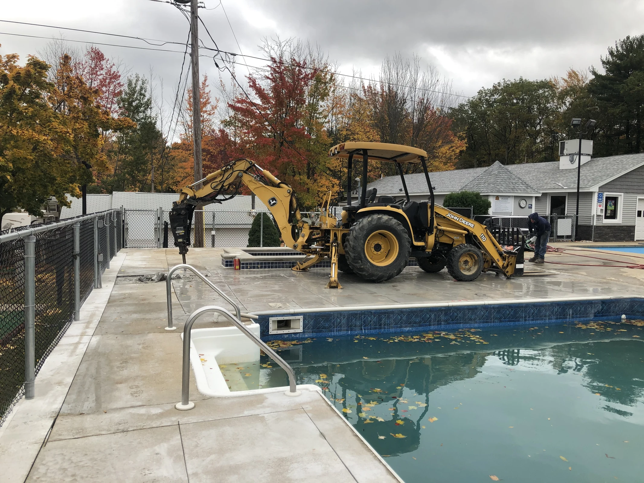 J-PAC Construction backhoe with a hydraulic breaker demolishing a concrete pool deck for removal