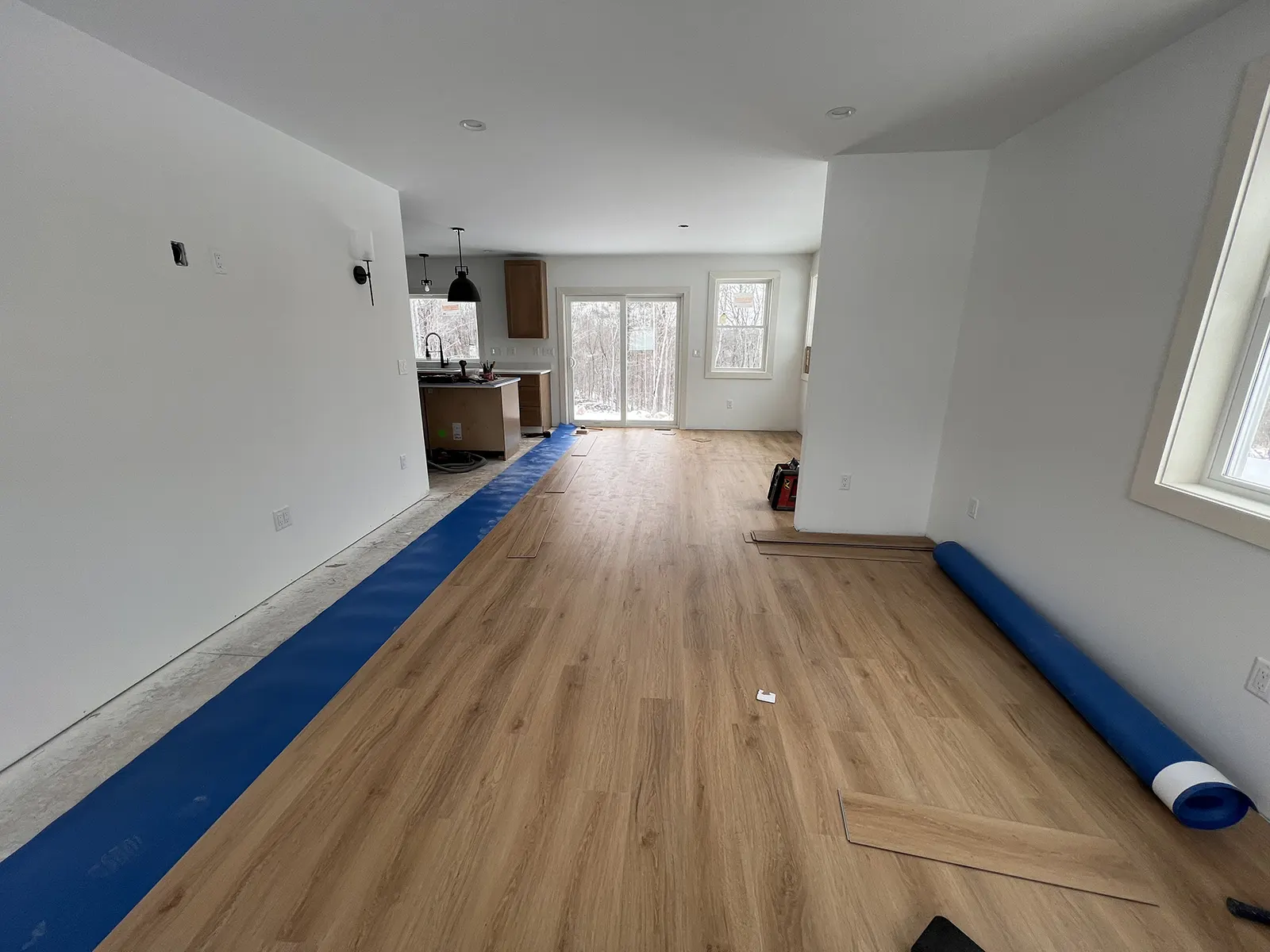 Luxury vinyl plank flooring being installed in an open-plan hallway leading to the kitchen