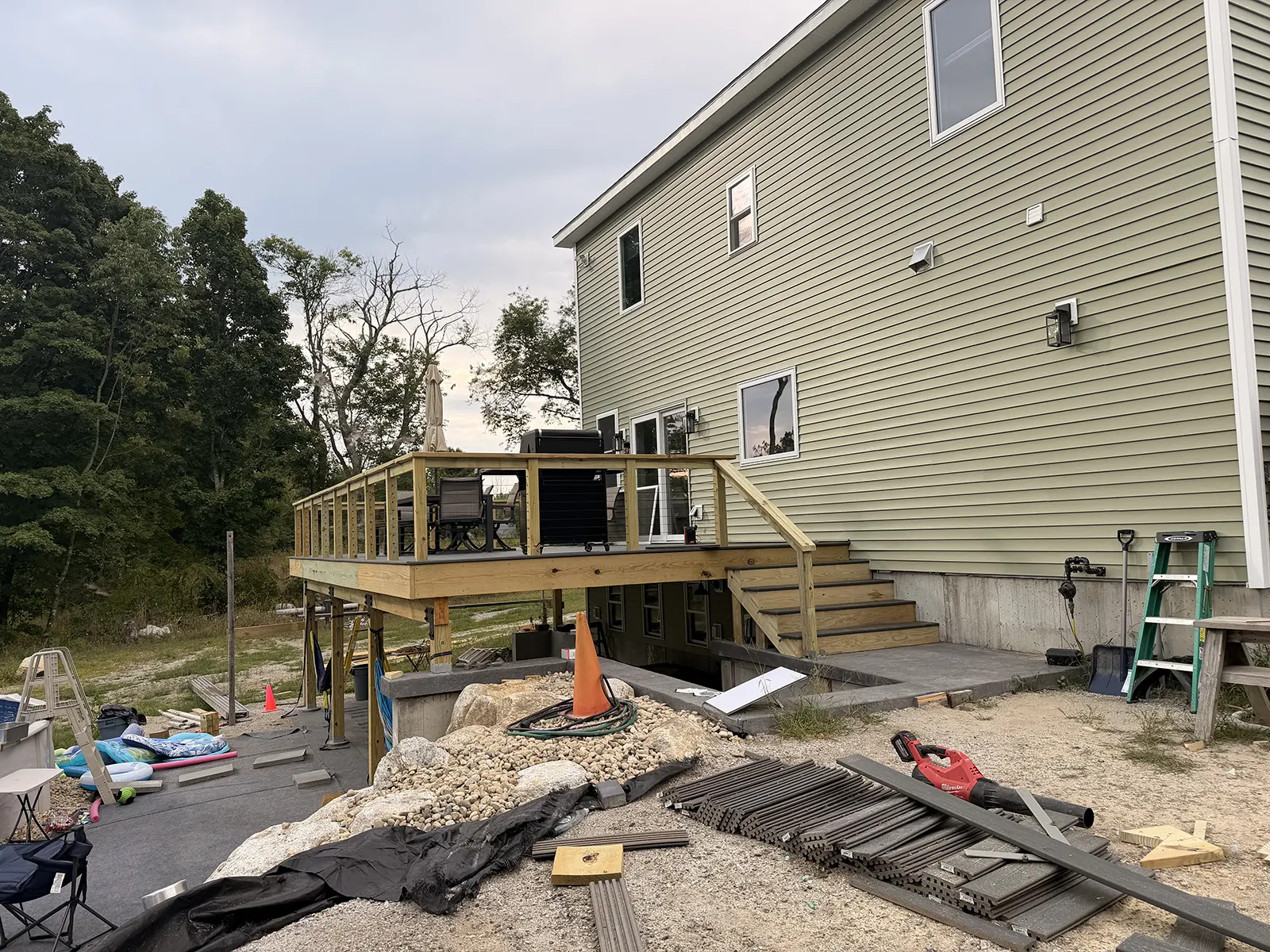 Two-story home with new green vinyl siding and a wood deck, with siding materials staged in the yard
