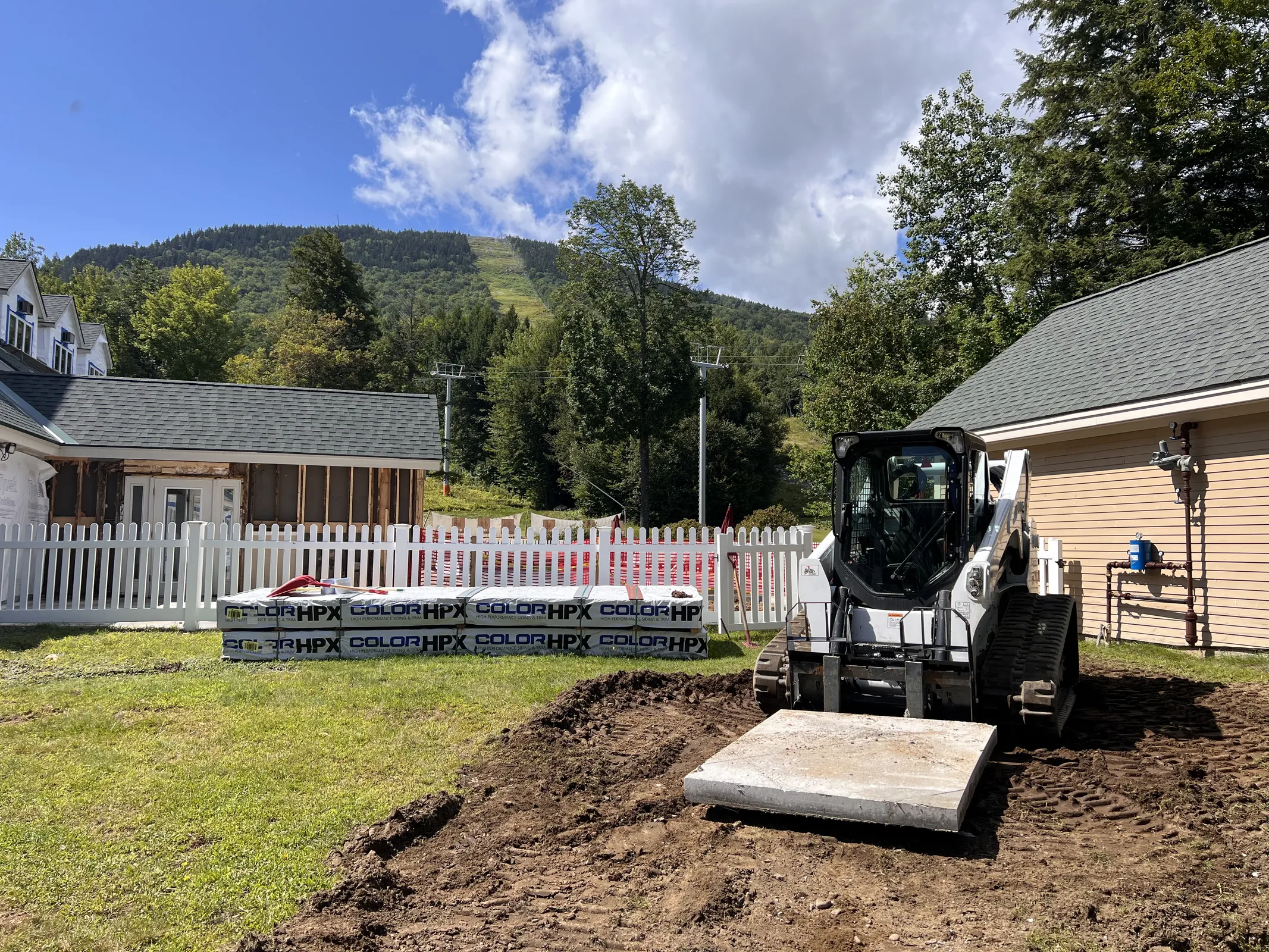 Compact track loader grading excavated soil beside a house to improve yard drainage
