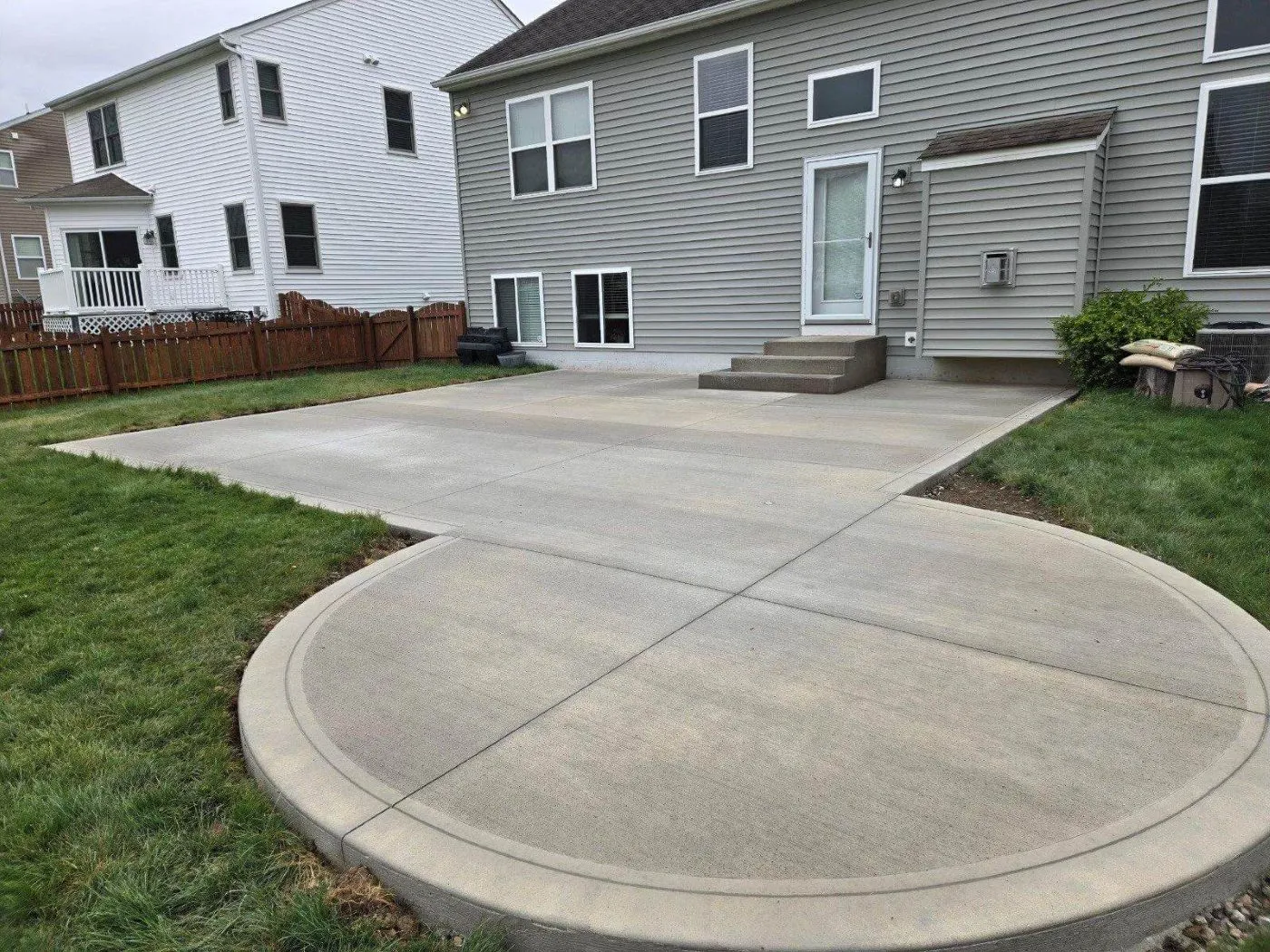 Broom-finished concrete patio with a curved circular extension behind a two-story home