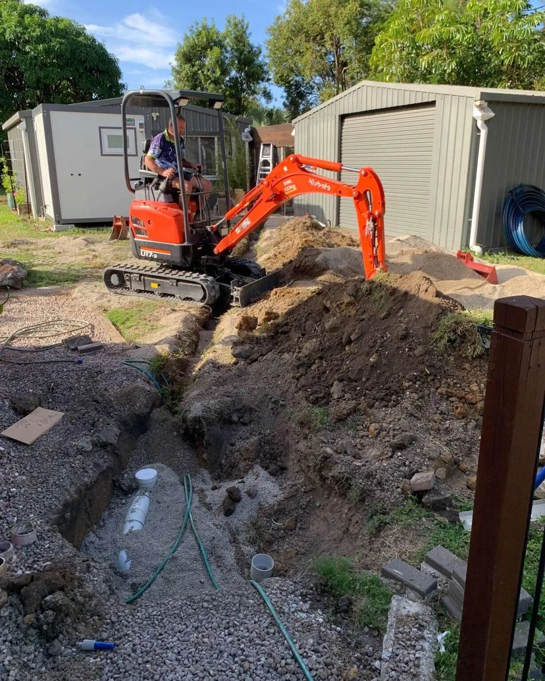 Mini excavator digging a drainage trench beside a backyard shed