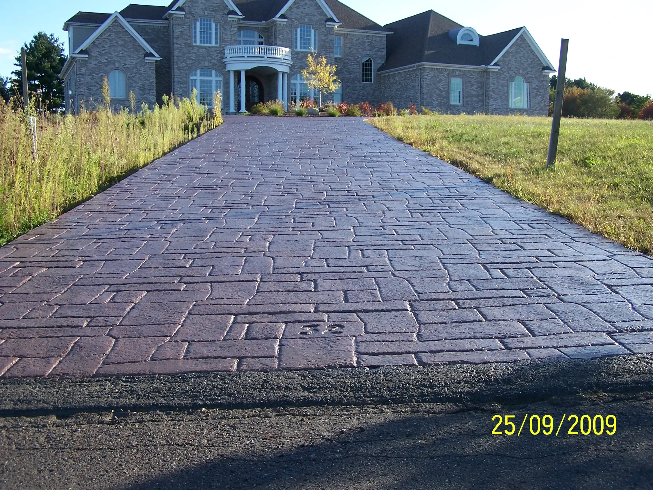 J-PAC Construction brick-red Appian cobblestone stamped concrete driveway leading to a stone home in Maine