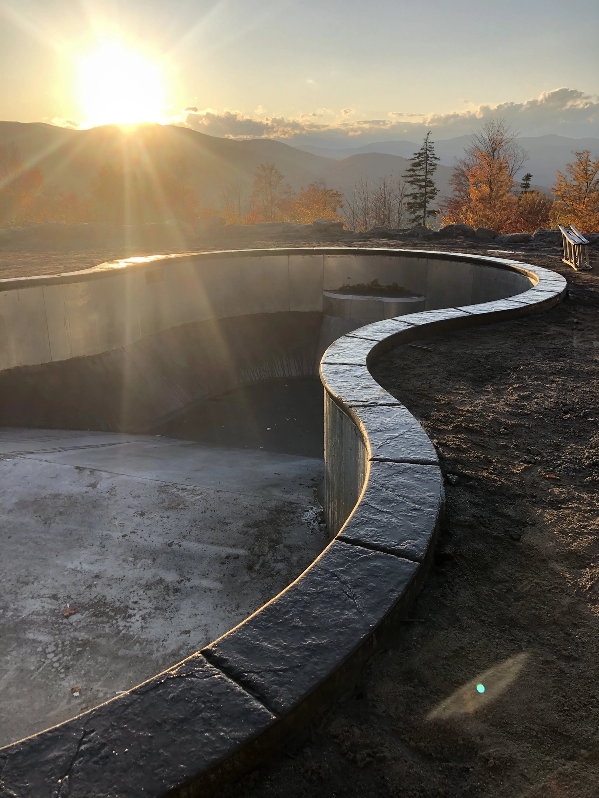 J-PAC Construction custom curved swimming pool coping stamped with old granite texture and dark charcoal release at sunset in Maine