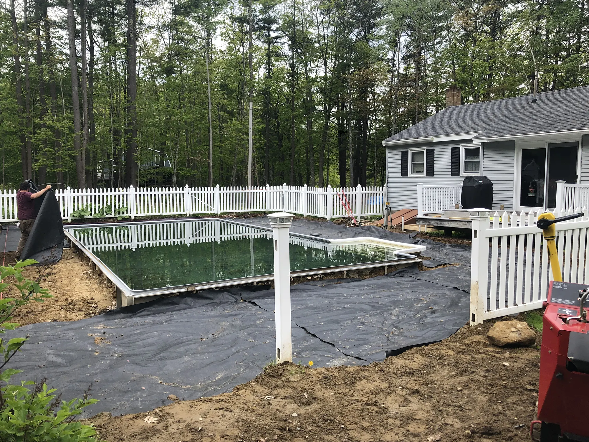 J-PAC Construction worker laying geotextile soil stabilization fabric during pool patio ground preparation in Maine