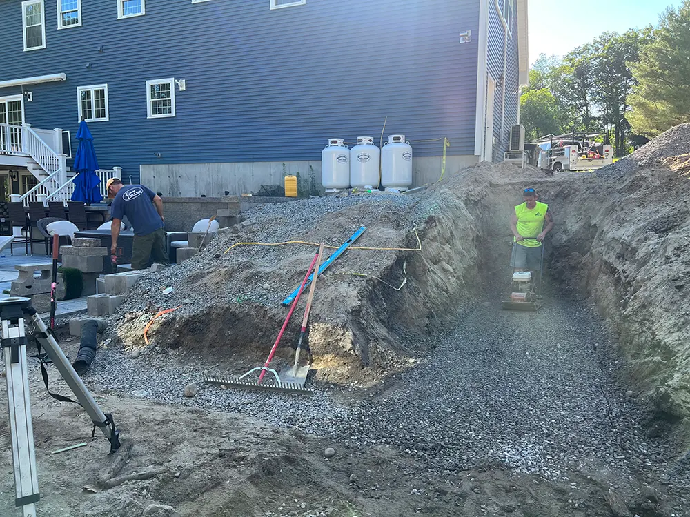 Crew compacting gravel base in excavated site with plate compactor