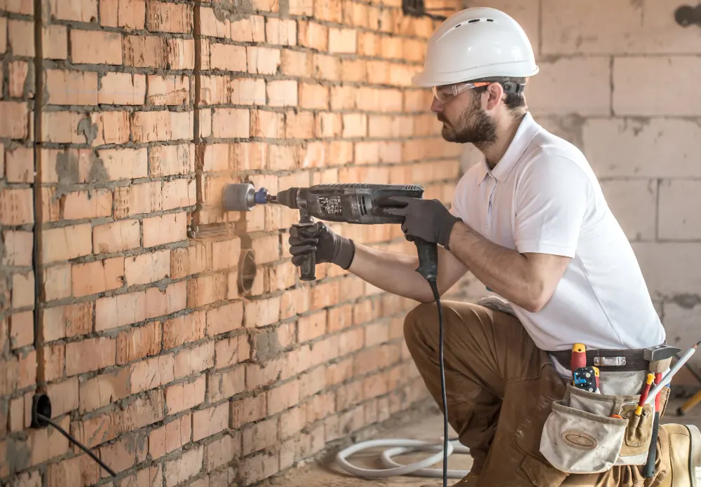 J-PAC Construction worker drilling brickwork during interior structural rot repair and masonry restoration in Maine