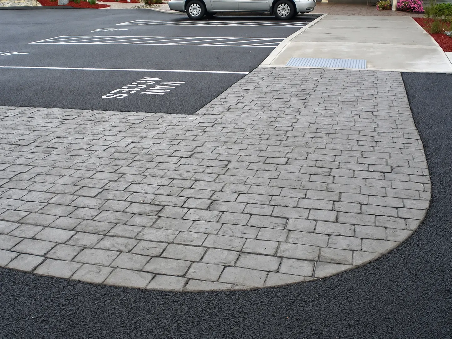 J-PAC Construction stamped cobblestone concrete walkway with an accessible curb ramp beside a parking lot