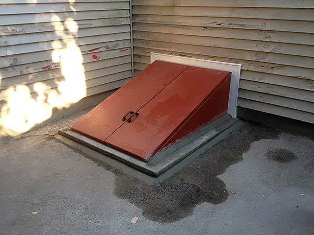 Red basement hatchway door installed on concrete exterior foundation for direct outdoor access